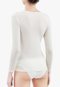 Top a maniche lunghe color crema con una texture liscia, scollo rotondo e design aderente, visto da dietro con una linea dell'orlo dritta.