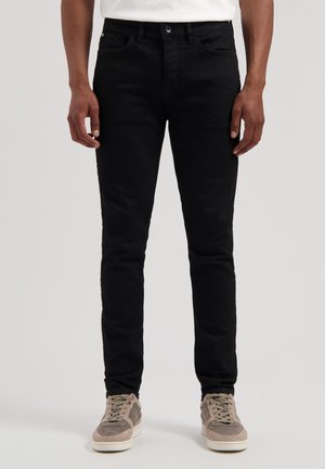 Jeans din denum negru, cu o croială slim, având un design clasic cu cinci buzunare, închidere cu nasture și detalii de cusătură subtile. Combinat cu adidași gri.