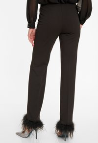 Zwarte op maat gemaakte broek met veren accenten aan de boorden, gecombineerd met puntige metallic hakken. Glad materiaal, slim fit, ontwerp tot op de grond.