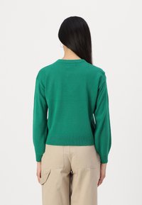 Grønn strikket genser med rund hals, ribbede mansjetter og hem. Stoffet virker glatt og lett, egnet for lagdeling.