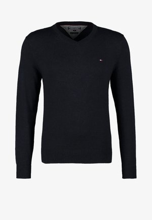 Maglione nero a scollo a V, jeans blu slim-fit, stivaletti marroni alla caviglia e una borsa a tracolla marrone. Tessuto resistente e design casual.