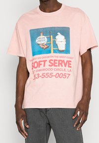 Muž v růžovém tričku s vintage nápisem na měkkou zmrzlinu a textem inzerujícím Cream Castle, včetně adresy a telefonního čísla.