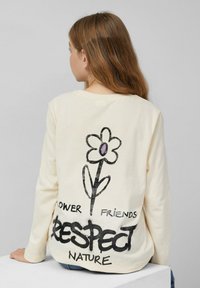 Langjarige crèmekleurige shirt met een bloemenafbeelding, zwarte tekst "RESPECT NATURE," en een zachte katoenen textuur.
