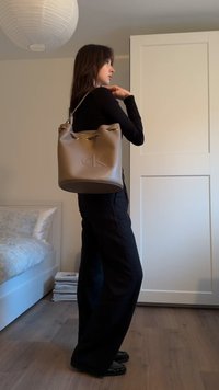 Sac seau beige en matière douce avec une finition texturée, doté d'une fermeture à cordon contrastante et d'un logo embossé.
