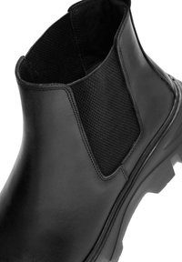 Botín Chelsea de cuero negro con un panel lateral elástico texturizado, suela resistente y acabado suave, que ofrece un diseño elegante y moderno.