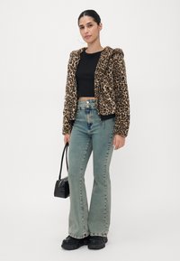Leopardmønster faux fur-jakke med en cropped design, svart tettsittende topp, høy midje lyseblå jeans og kraftige svarte platformsko.