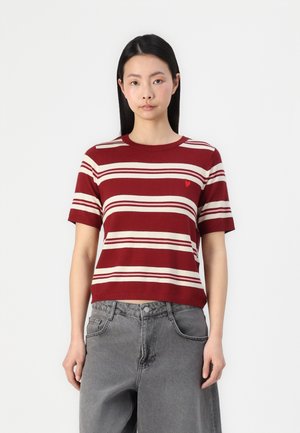 Haut en tricot à rayures rouges et beiges, à manches courtes, avec un col rond et un petit logo en forme de cœur rouge sur la poitrine gauche. Coupe décontractée.