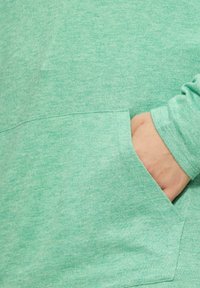 Mintgrüner Pullover aus weichem, strukturiertem Stoff mit einer Fronttasche und eng anliegenden Ärmeln.