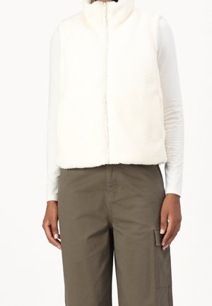 Person iført en hvid fleecevest med lynlås over en langærmet hvid skjorte og olivengrønne cargobukser med sidelomme.