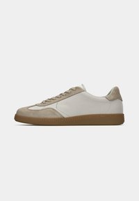 Beige en witte sneakers met een bovenwerk van suède, een gladde rubberen zool en vetersluiting. Heeft tonale stiksels langs de zijkanten.