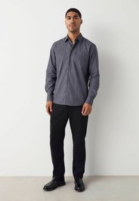 Geruit overhemd met knopen in navy en wit, lange mouwen, gedragen met zwarte broek en zwarte schoenen, tentoongesteld op een mannelijke mannequin.