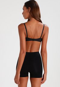 Svart bh med justerbare stropper og hakefeste, kombinert med høy midje svarte shorts, begge laget av glatt, elastisk stoff.