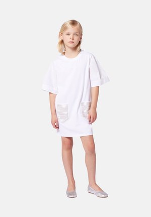 Robe en coton blanche à manches courtes, dotée de deux poches en métal argenté texturé. Associée à des ballerines argentées. Style simple, coupe décontractée.