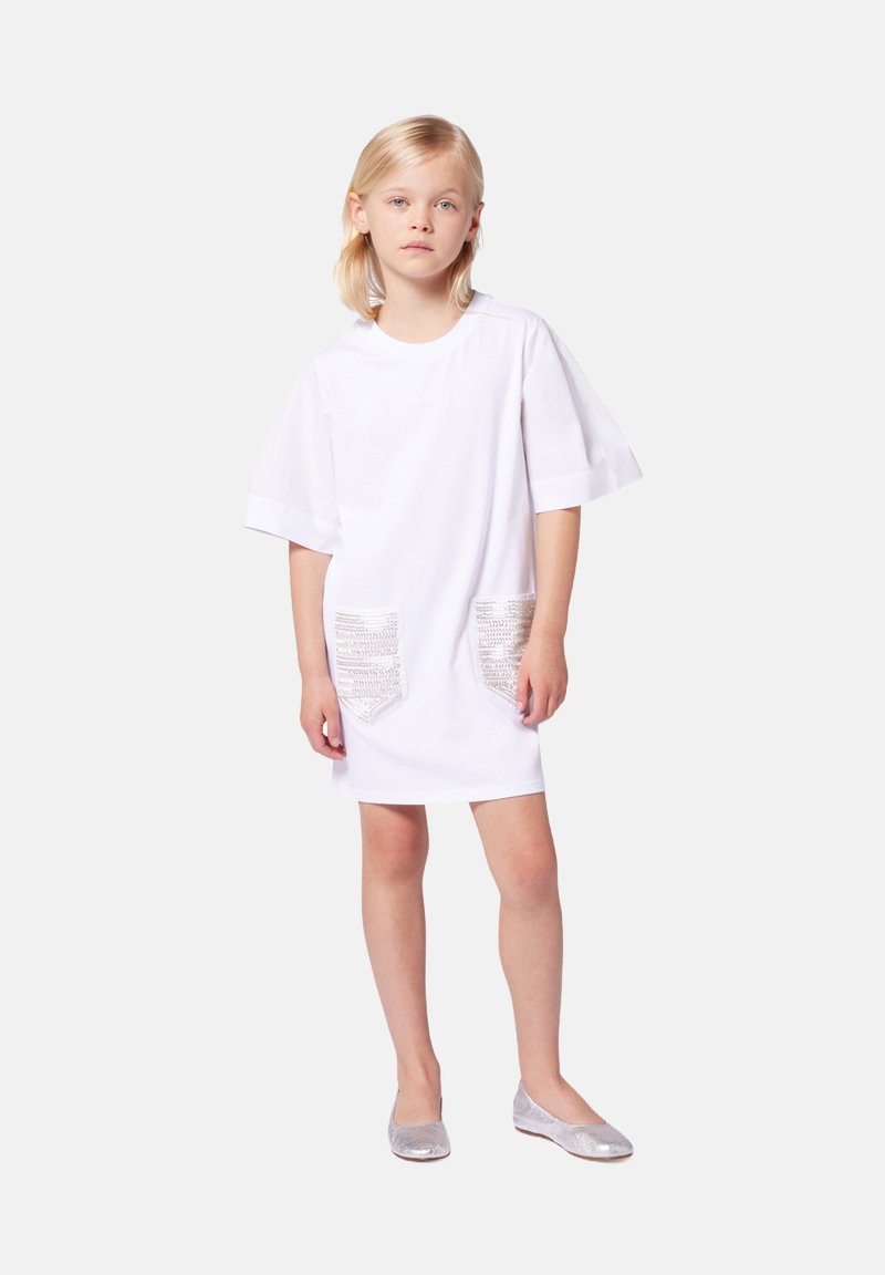 Robe en coton blanche à manches courtes, dotée de deux poches en métal argenté texturé. Associée à des ballerines argentées. Style simple, coupe décontractée.