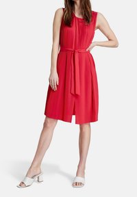 Punainen poimutettu mekko, jossa on istuva bodice ja vastaava vyötärönauha. Pituus on polveen saakka, ja se on valmistettu sileästä, kiiltävästä kankaasta sekä on olkaimeton.
