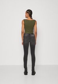 Ribbet olivengrønn tanktopp kombinert med tettsittende mørkegrå jeans. Modellen har på seg svarte ankelstøvler og viser antrekket fra bak.