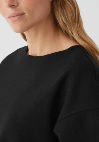 Zwarte sweatshirt met een ronde hals, zachte textuur en minimalistisch ontwerp. Beschikt over een verlaagde schouderlijn en een soepele afwerking.