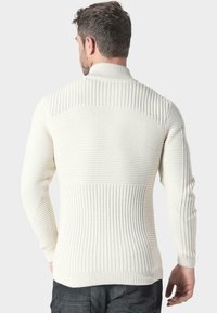 Jersey de punto en blanco roto con textura acanalada, cuello alto y panel contrastante en los hombros. Diseño ajustado con mangas largas.