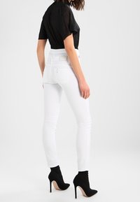 Jeans blancos ajustados de cintura alta, combinados con tacones negros estilo calcetín. La parte superior es de un tejido negro transparente con mangas cortas.