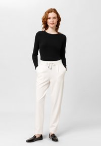 Zwarte lange mouwen top gecombineerd met crèmekleurige op maat gemaakte broeken met een trekkoord, zijzakken en een gladde textuur. Zwarte instapschoenen maken de look compleet.