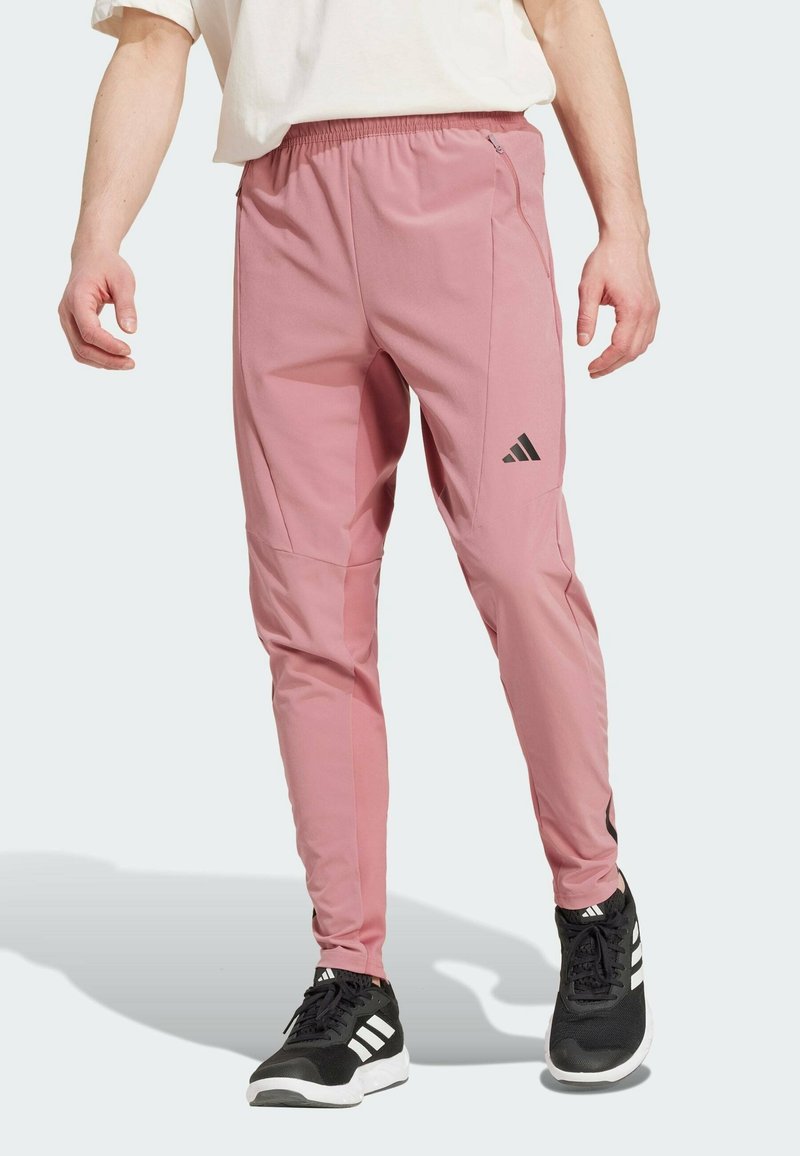 Rosa Sporthose mit elastischem Taillenbund, mit Reißverschlüssen versehenen Taschen und schwarzen Logo-Akzenten. Aus glattem Stoff, mit schmal zulaufendem Bein.
