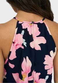 Květinový halter top v námořnické tkanině s růžovými květinovými vzory. Má klíčovou knoflíkovou úpravu na zadní straně a texturovaný, lehký design.