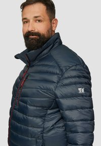 Dunkelblaue Daunenjacke mit gestepptem Design, hohem Kragen und roten Reißverschlussakzenten. Verfügt über ein Logo am linken Ärmel. Angenehme Oberfläche.