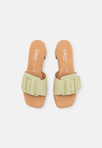 Gröna sandaler med sidskaft har ett brett rem med spänne, en tan dämpad innersula och en låg klack. Slät textur genom hela sandalen.