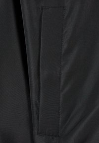 Tissu noir avec une texture lisse et un patch rectangulaire cousu à la surface. Le matériau semble léger et durable.