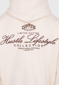 Beżowa bluza z kapturem z brązowym napisem "Dropsize 2020", "Edycja Limitowana", "Kolekcja Lifestyles Hustle" oraz "Dropsize Oryginalna Moda Uliczna Założona w 2020".