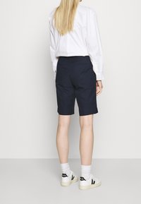 Námořnické přizpůsobené kraťasy s čistými liniemi, končící nad kolenem, spárované s bílou košilí s dlouhým rukávem a bílými teniskami.