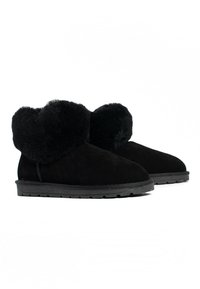 Botas de tobillo de ante negro con un suave acabado de piel de pelaje en el puño, punta redondeada, suelas de goma planas y una superficie texturizada.