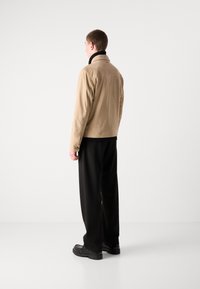 Beige leather jacket with a collar, shown from the back. The model wears black wide-leg trousers and chunky black shoes. Smooth texture.