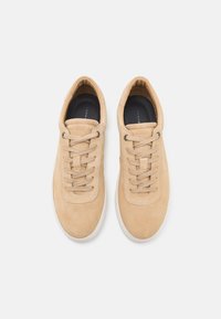 Beige suede sneakers with a rounded toe, lace-up design, and contrasting white rubber sole. Soft texture with subtle stitching details.