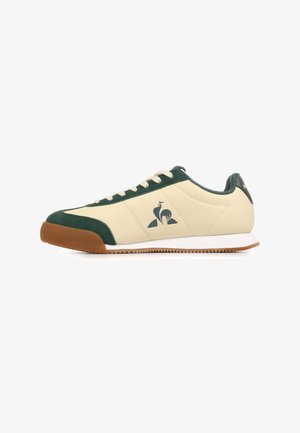 Sneaker crema dal profilo basso con dettagli in camoscio verde scuro, lacci bianchi, suola in gomma e logo scuro sul lato.