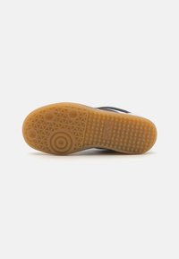 Sneaker nera con suola in gomma texturizzata, dotata di una suola in gomma marrone chiaro e motivi di trazione circolari per una migliore aderenza.