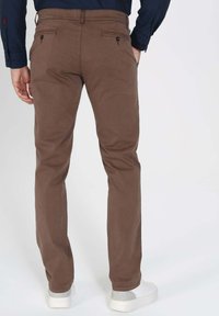 Pantalons en coton marron avec une coupe droite, dotés de poches arrière avec des boutons et portés avec des baskets blanches.