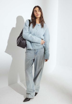 Cárdigan esponjoso de un azul claro con botones, combinado con unos jeans sueltos de un azul claro y zapatos de punta negra; la modelo lleva un bolso tote negro.