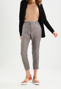Gray cropped trousers with a smooth texture, button closure, and front pockets, paired with a tan sweater and color-blocked slip-on shoes.