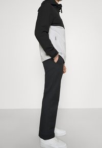 Lehká černá a šedá bunda s kapucí, se zipovou kapsou, v kombinaci s oblekovými černými kalhotami a bílými teniskami.