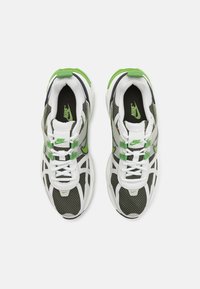 Zapatillas de malla blancas y grises con detalles en verde, que presentan un upper texturizado, sistema de cordones y una suela negra en contraste. Logotipo de Nike visible.