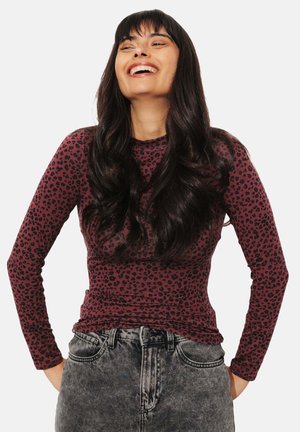Haut à manches longues bordeaux avec un motif léopard noir ; tissu doux, coupe ajustée, col rond, porté avec un jean gris taille haute.
