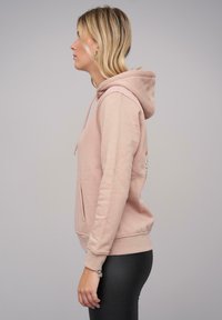Felpa rosa in cotone con tasca frontale, cappuccio con cordino e polsini a costine, che mostra un design semplice e una texture morbida.