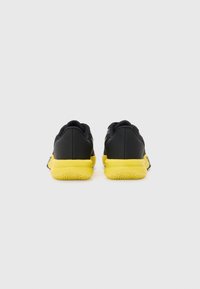 Des chaussures de sport noires et jaunes présentent un dessus texturé, un col rembourré et une semelle extérieure en caoutchouc avec une grippe à motifs pour améliorer l'adhérence.