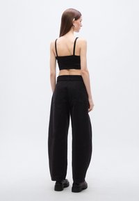 Μαύρο cropped τοπ με λεπτές τιράντες συνδυασμένο με μαύρο παντελόνι φαρδιάς γραμμής. Το παντελόνι έχει τσέπες και ελαφρώς υφή στην επιφάνειά του.