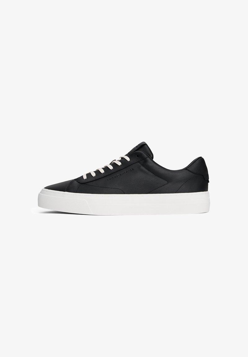 Black leather sneaker with white rubber sole, rounded toe, and contrasting white laces. Features minimalist design and tonal stitching.