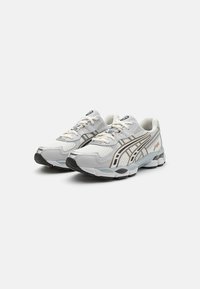 Asics skriešanas apavi gaiši pelēkā krāsā ar acs un sintētisku augšdaļu, melnu gumijas zoli, baltām šņorēm un metalizētām sudraba akcentiem.