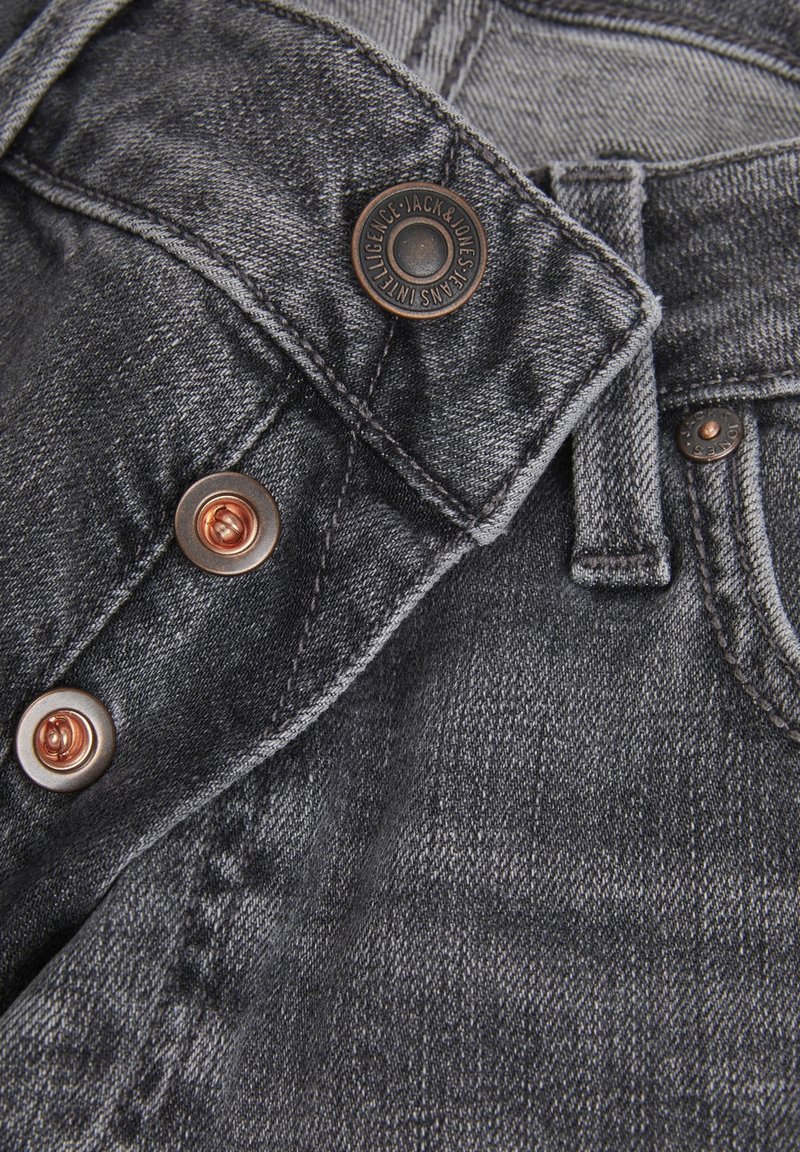 Jeans de denim negro con un acabado texturizado, que presentan herrajes de cobre y costuras decorativas en la cintura y los bolsillos.