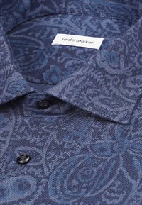 Chemise bleue à motifs, boutonnée, avec un col et des boutons noirs, comportant une étiquette de marque "seidensticker" visible à l'intérieur du col.