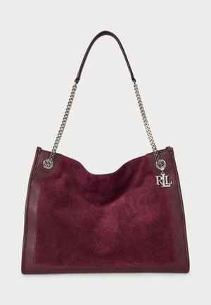 Bordeaux suède handtas met leren afwerking, brede opening, zilveren kettingband en logo-hanger detail. Zachte textuur en modern ontwerp.
